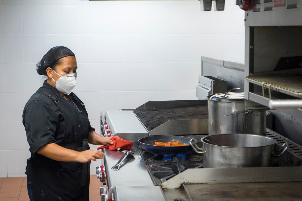 Chef busy at work in a commercial kitchen, preparing dishes while wearing a protective mask.
